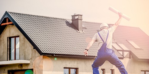 Eine Person springt vor einem Haus mit einem Bauplan